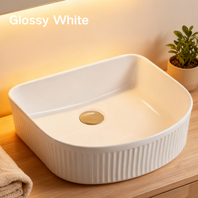 Modern glossy white fluted vessel sink with gold pop-up drain on a wooden bathroom countertop.